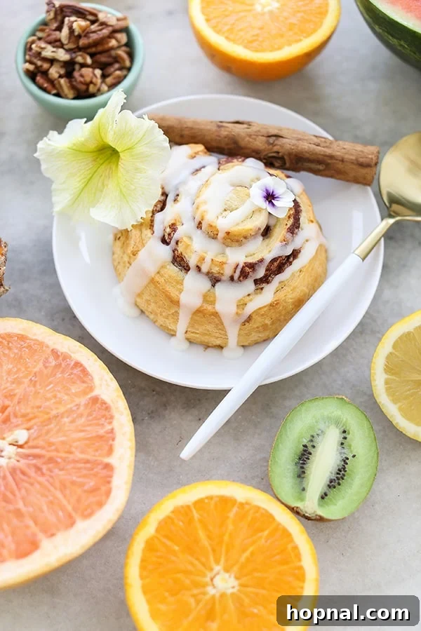 Effortless Brunch Bliss 3 A perfectly golden cinnamon roll adorned with edible flowers, resting on a white plate with fresh fruit artfully arranged around it.