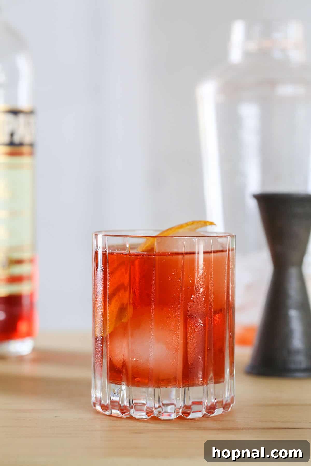 Negroni cocktail served with a large, clear ice cube and an orange peel garnish, highlighting its refreshing quality.