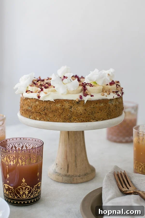 Super Moist Banana Cake Made with Oil 6 A beautifully frosted banana cake on a cake stand, garnished with fresh banana slices, ready to be enjoyed.