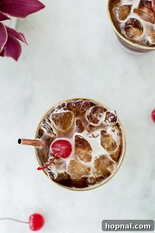Overhead shot of a coffee tonic, featuring a vibrant red maraschino cherry on top, sitting on a clean background.
