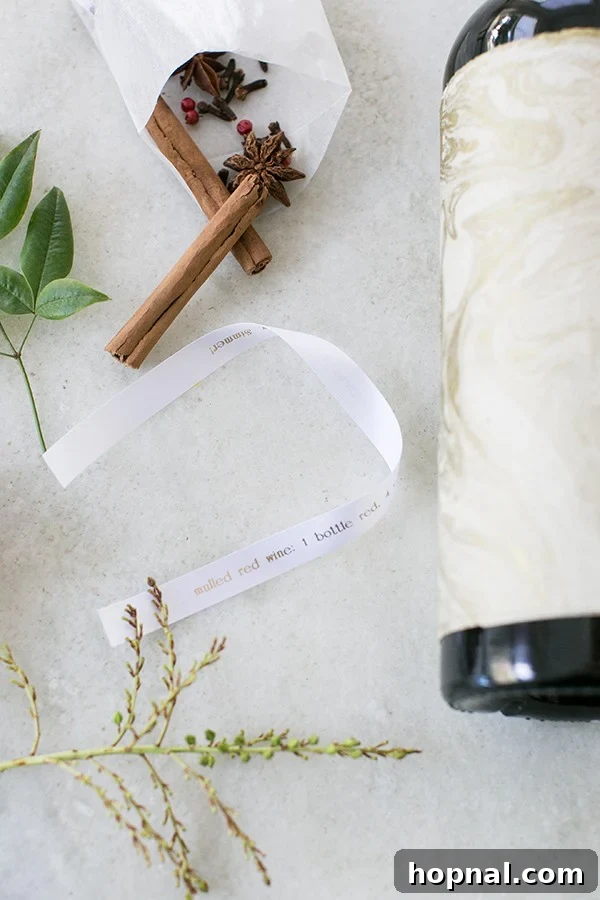 A festive arrangement of wine, ribbon, and mulling spices, hinting at a DIY mulled wine kit, on a marble surface.