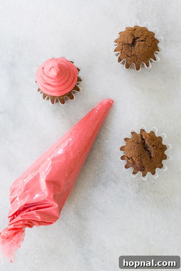 Close-up of a hand frosting a gingerbread cupcake with red buttercream to create a Santa hat.