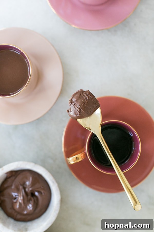 Hazelnut Cocoa Indulgence 7 A spoon delicately holding a rich dollop of Nutella hovers over a steaming cup of coffee, poised to enhance the beverage with its creamy, chocolatey hazelnut goodness.