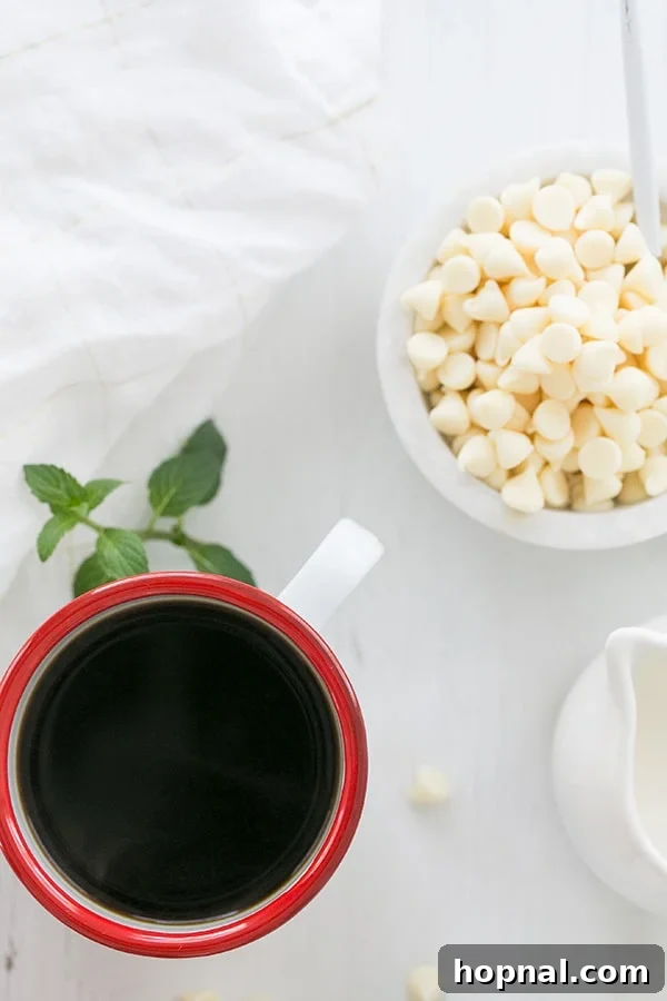 A close-up of a cup of freshly brewed coffee, garnished with white chocolate chips on a rustic surface, emphasizing warmth and indulgence.