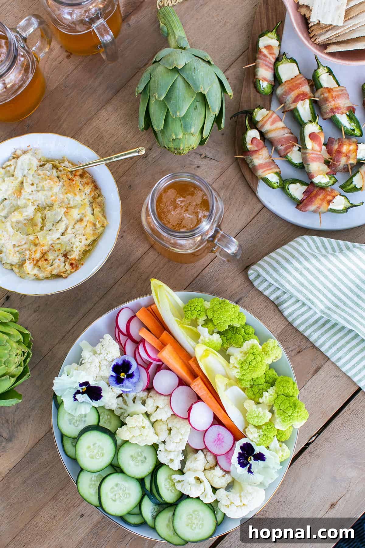 Cheesy artichoke dip served hot in a baking dish, surrounded by fresh vegetable sticks for dipping.