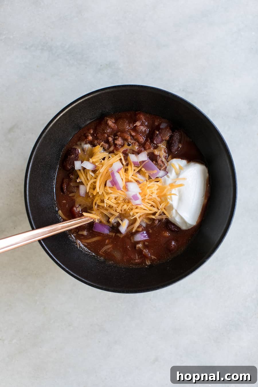 A steaming bowl of the best slow cooker chili, garnished with cheese and fresh cilantro.