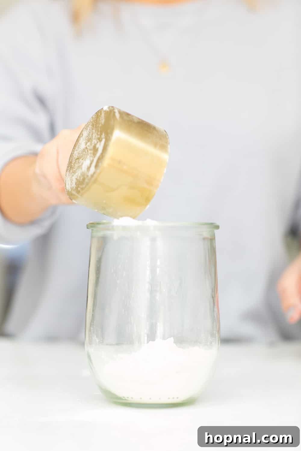 Pouring flour carefully into a glass jar as part of the layering process for cookie mix.