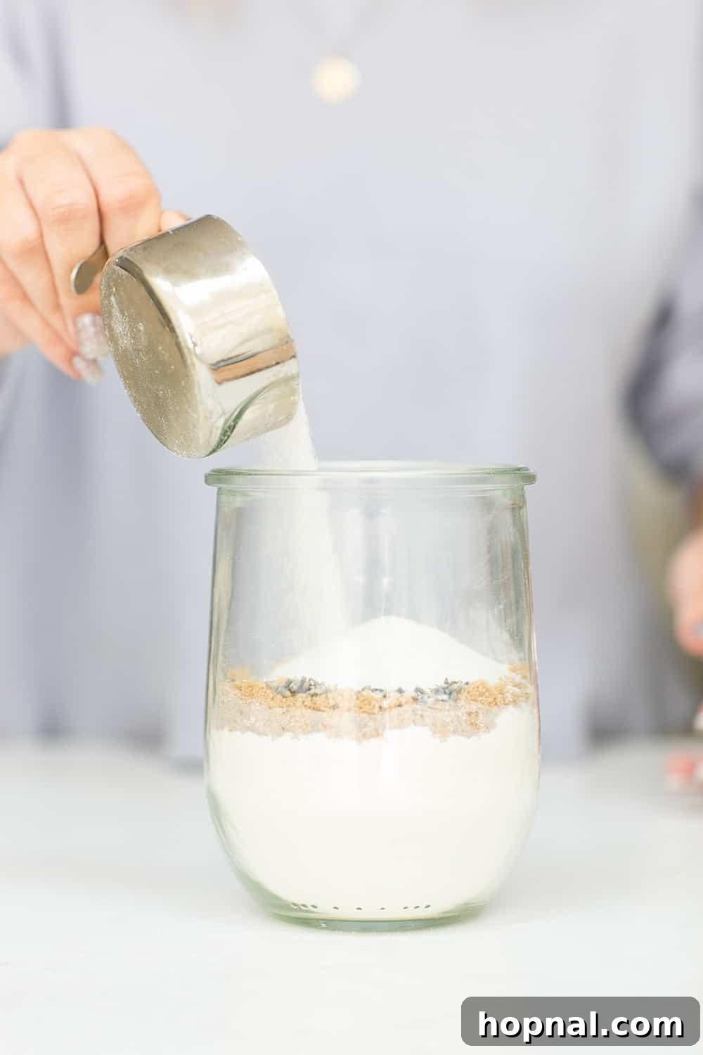 Layering various dry ingredients, including sugars and possibly lavender, into a glass jar.