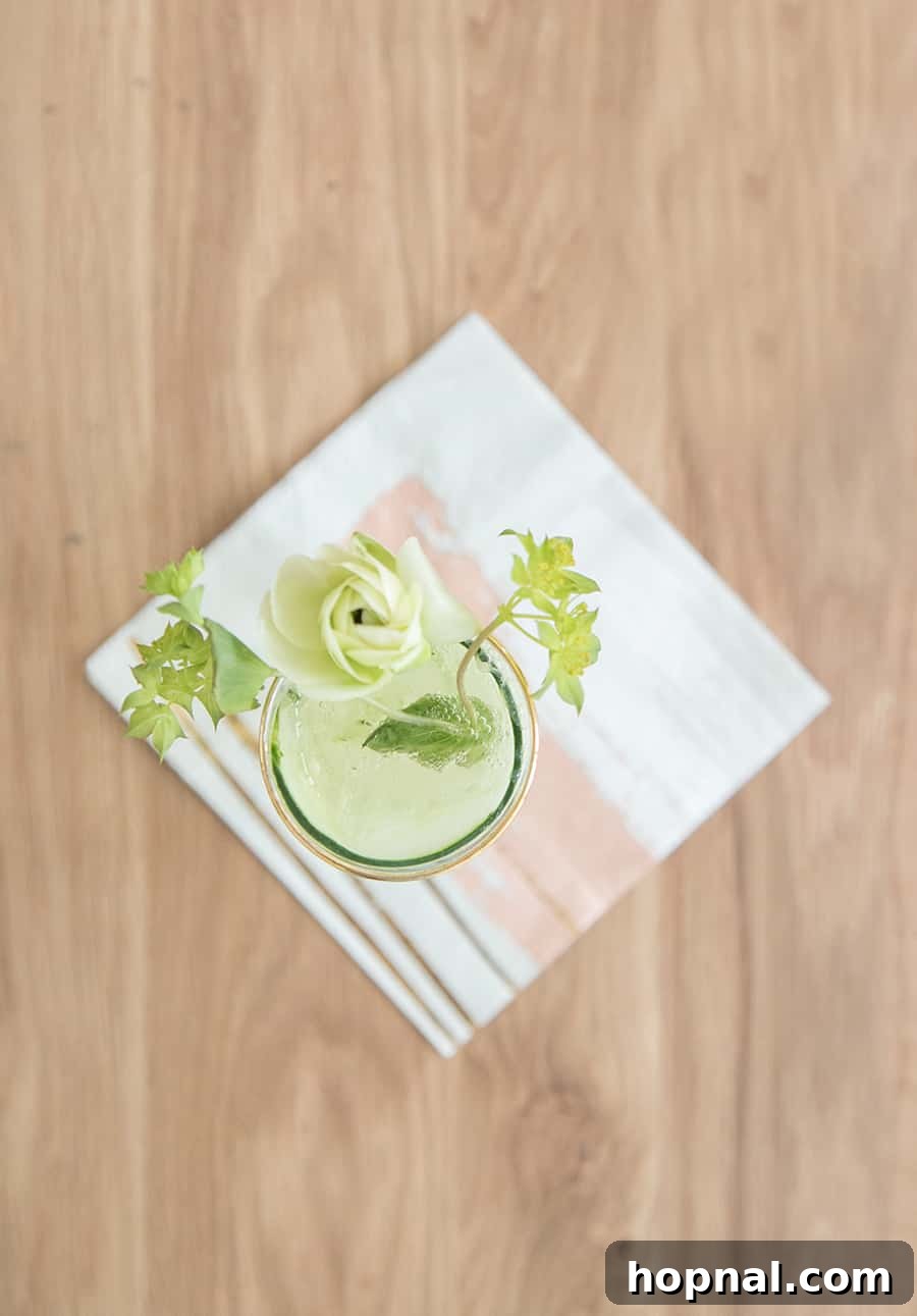 Refreshing Cucumber and Kiwi Gimlet Recipe 2 Refreshing Cucumber and Kiwi Gimlet cocktail served on a rustic wooden table with decorative spring flowers and a linen napkin, highlighting its vibrant green color.