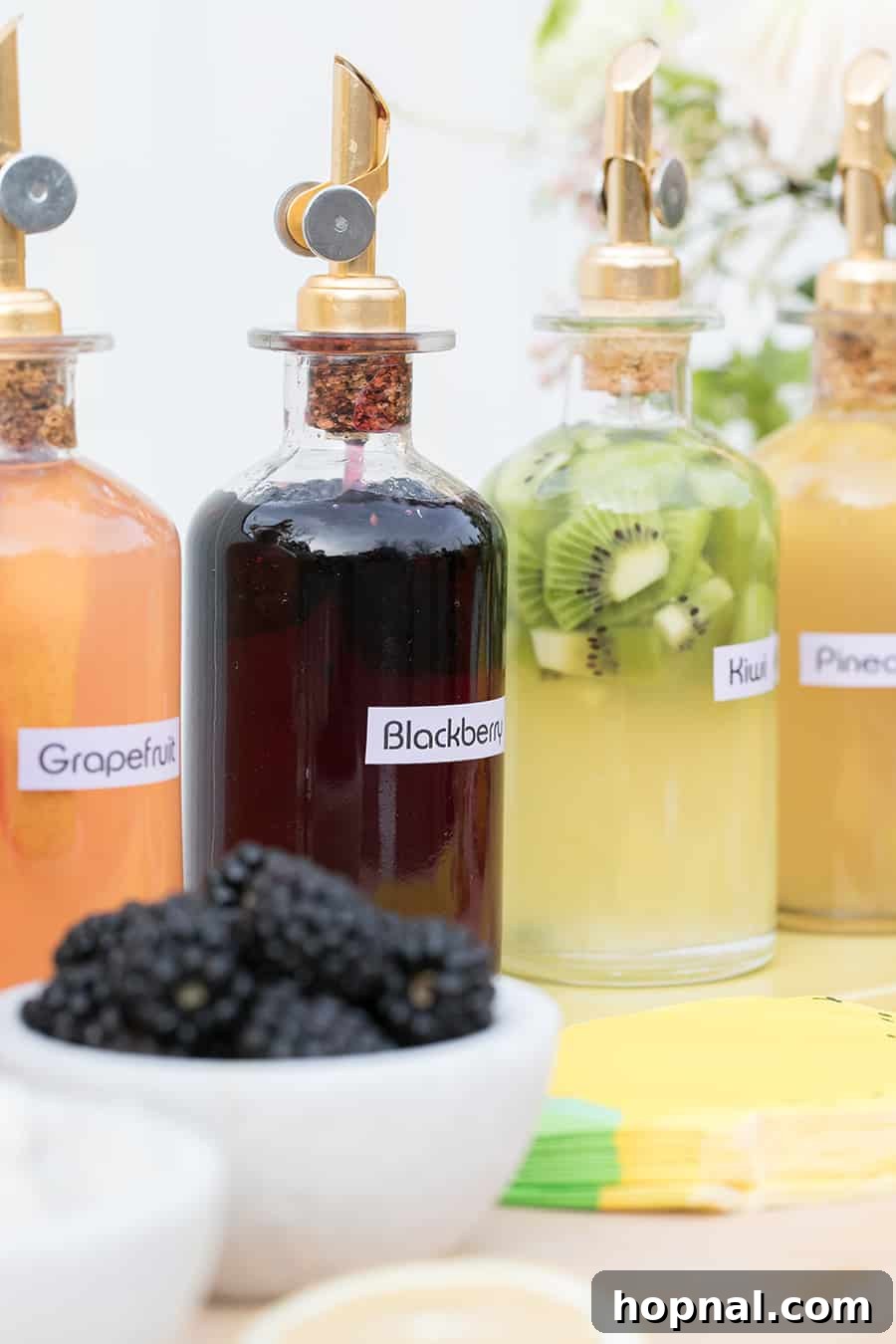 A collection of beautifully bottled homemade fruit syrups, featuring elegant gold pour spouts, meticulously arranged for a sophisticated lemonade bar.