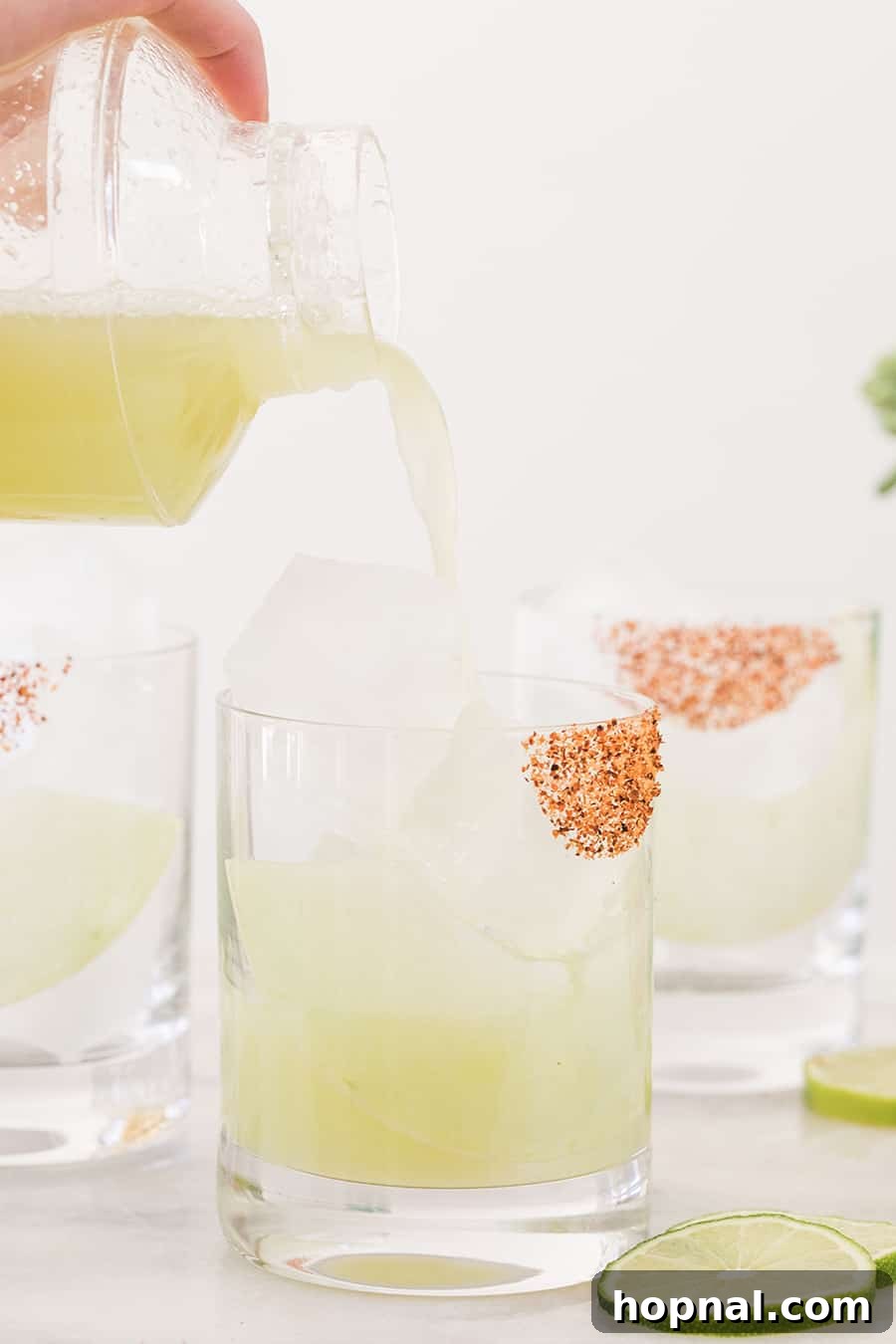 Pouring a vibrant honeydew margarita from a clear cocktail shaker into a salt-rimmed glass filled with ice, ready to serve.
