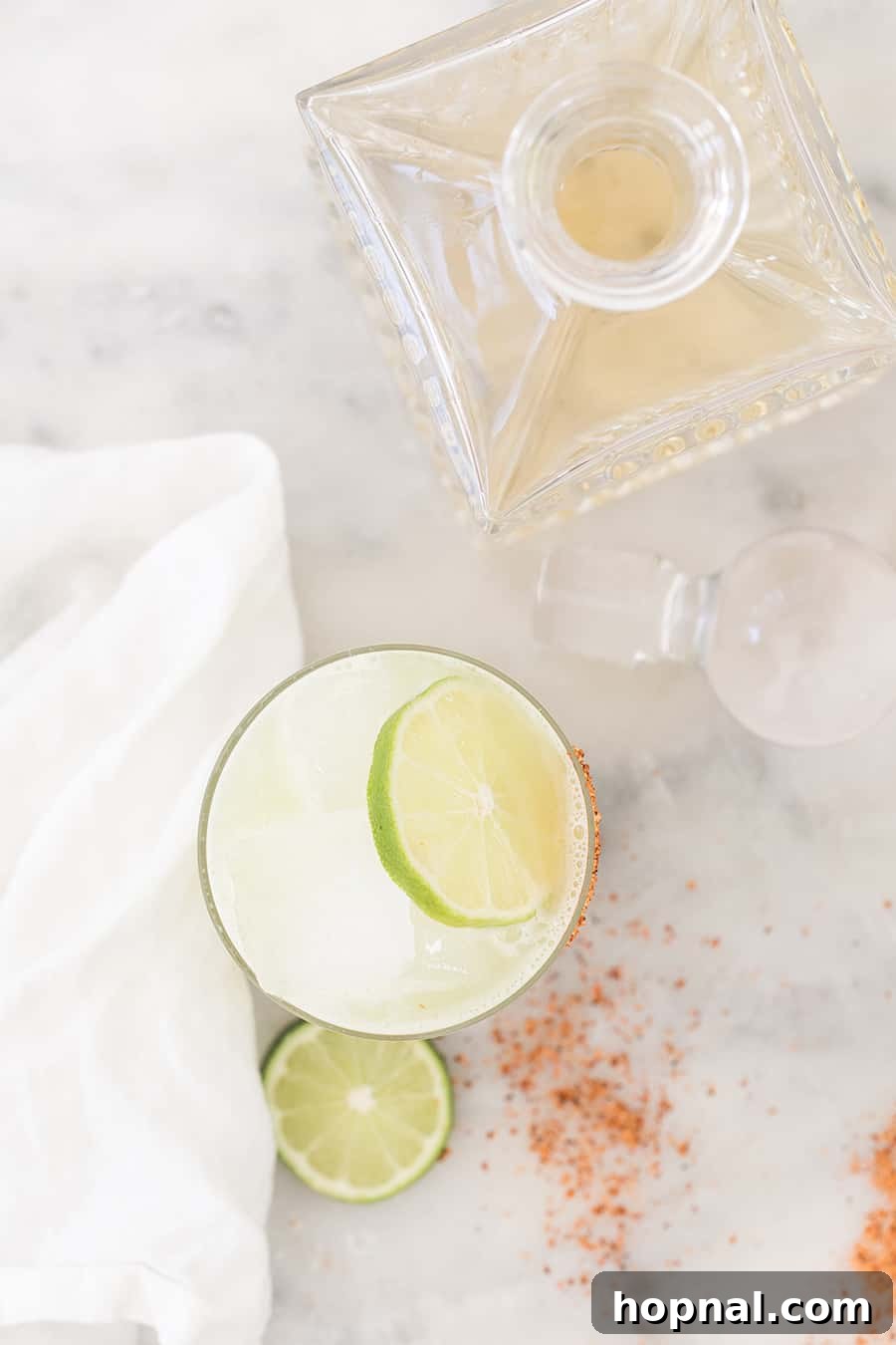 A beautifully prepared cocktail in a lowball glass, garnished with a lime wedge, next to a bottle of premium tequila.
