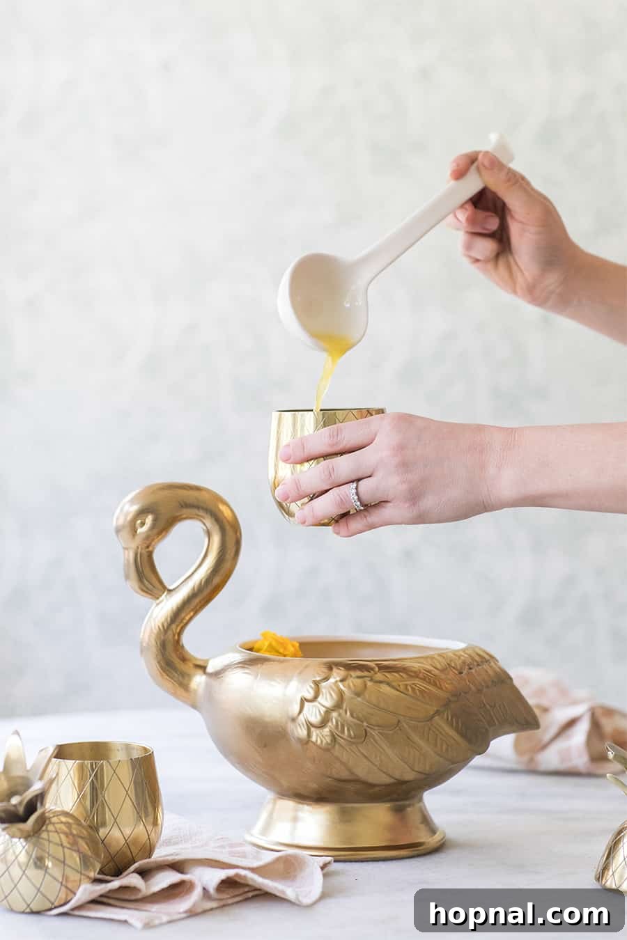 Overhead shot of a hand using a ladle to scoop tropical punch from a bowl into an elegant glass
