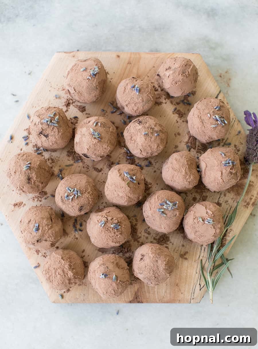A vibrant flat lay showcasing the key ingredients for dark chocolate lavender truffles: rich dark chocolate chunks, a bowl of heavy cream, and a generous bunch of fresh culinary lavender blossoms.