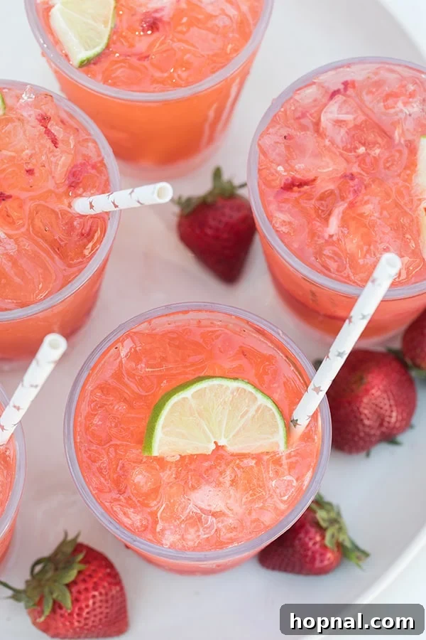 Top-down view of several strawberry tequila sodas in glasses, garnished with lime and strawberries.