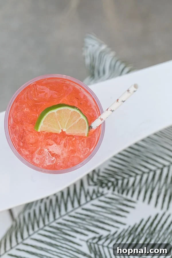 A refreshing summer cocktail, possibly a strawberry tequila soda, in a glass with ice and garnishes.