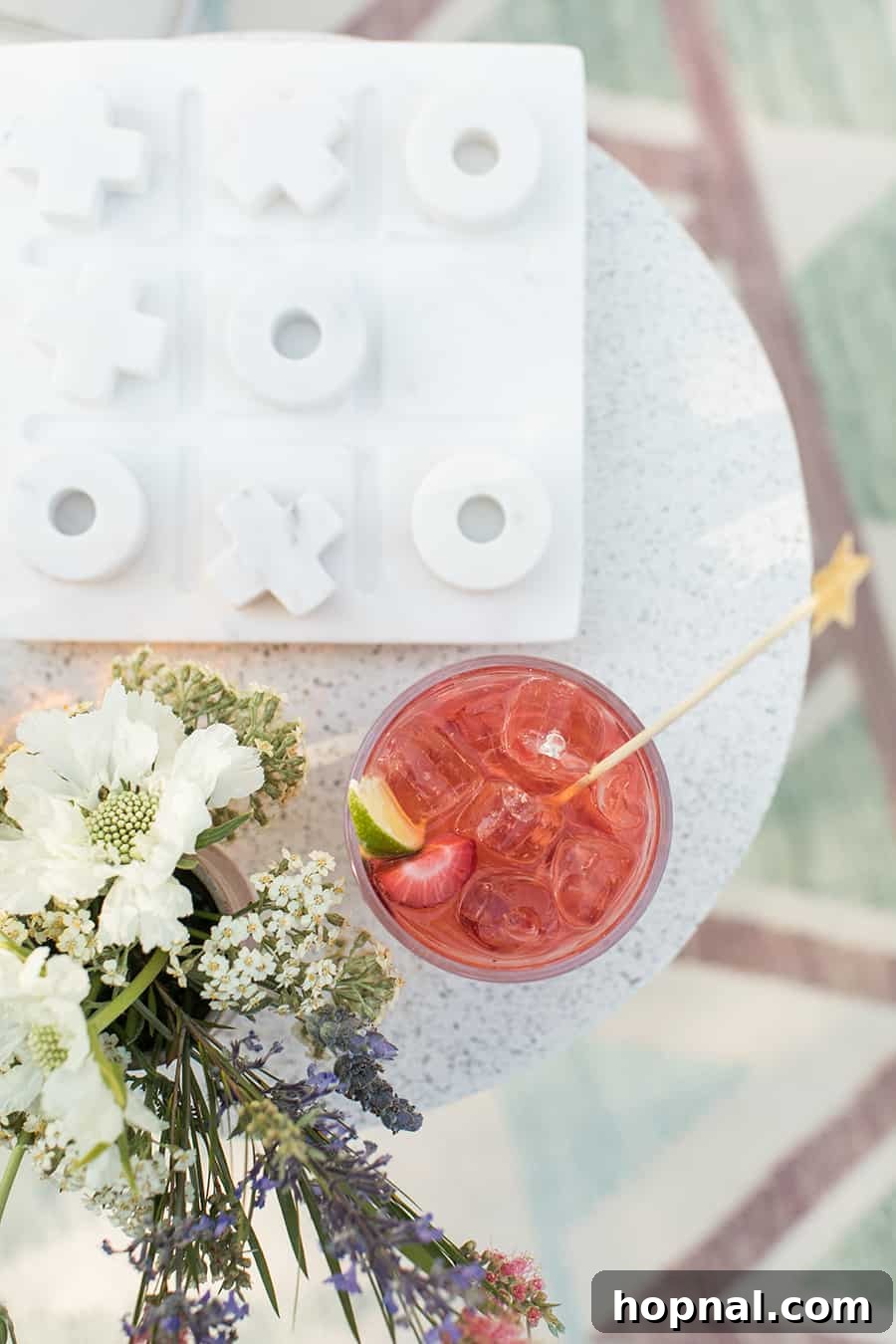 Lights, Camera, Backyard: Your Outdoor Movie Night Guide 2 A vibrant red cocktail on a table, surrounded by fresh flowers and a classic tic-tac-toe board, setting a relaxed outdoor mood.