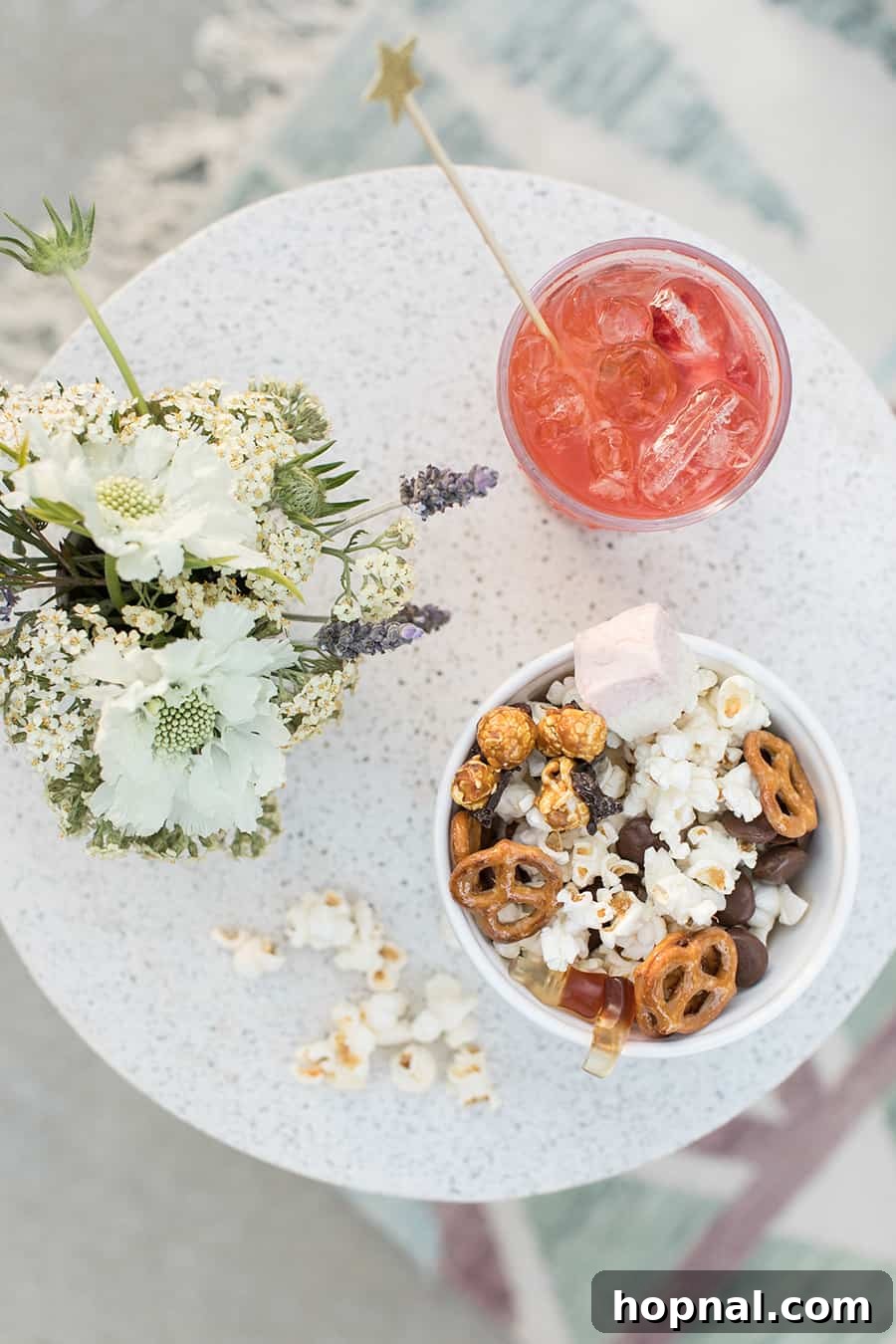 Lights, Camera, Backyard: Your Outdoor Movie Night Guide 13 An overhead shot of a red cocktail and a bowl of popcorn with decorative flowers on an outdoor table, perfect for a movie night.