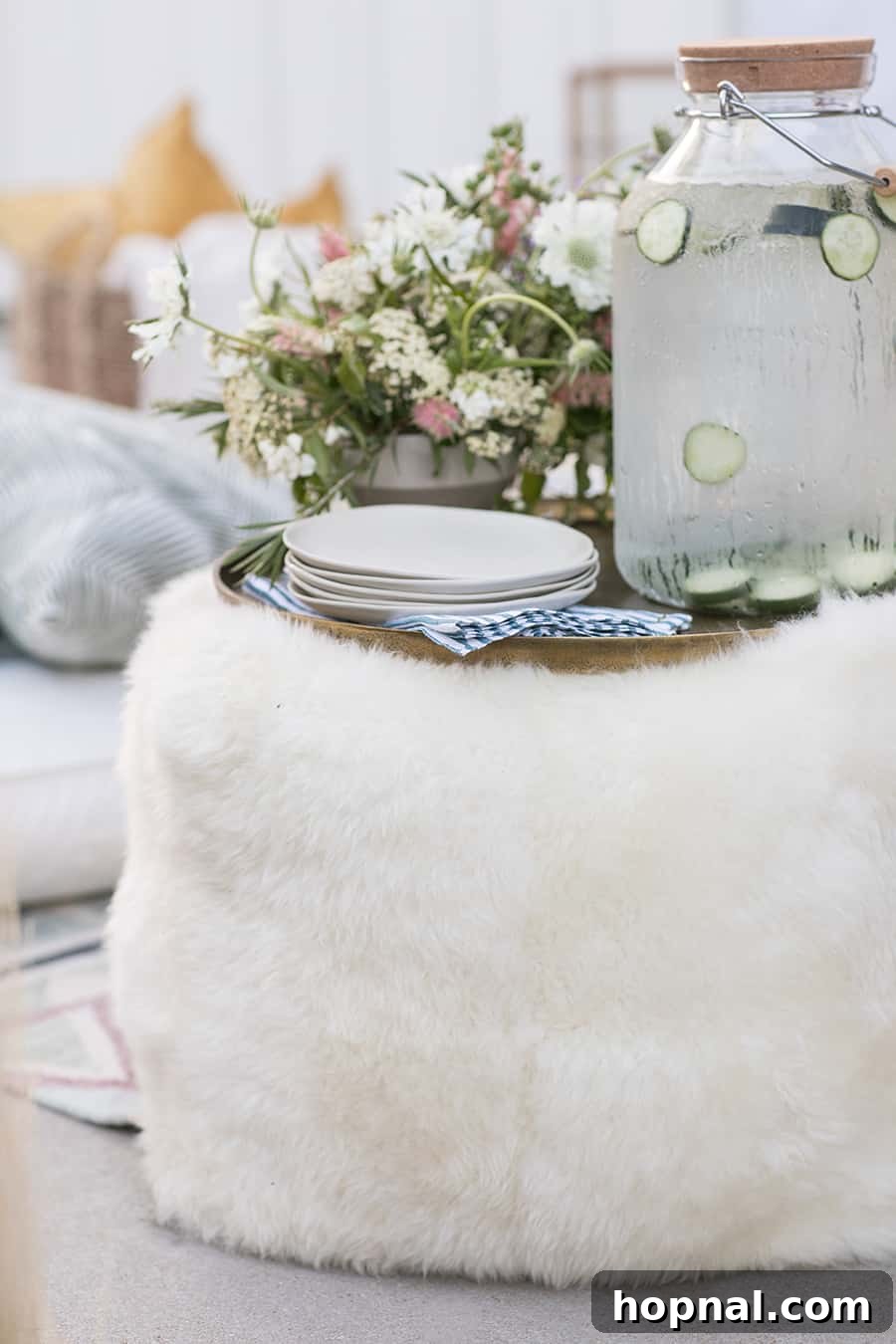 Lights, Camera, Backyard: Your Outdoor Movie Night Guide 10 A white pillow pouf adorned with a gold tray, plates, and a glass of water, serving as a chic and functional outdoor side table.