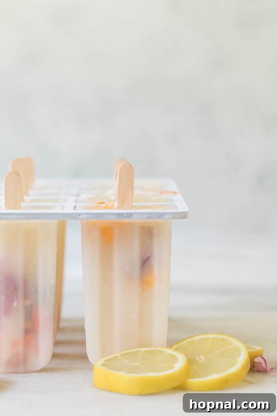 Lemonade popsicles nestled in a popsicle mold, garnished with vibrant edible flowers, ready for freezing.
