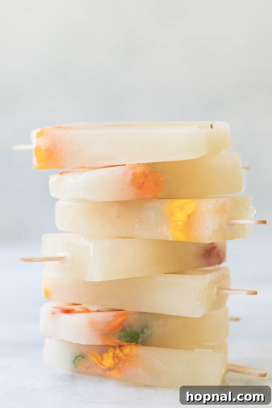 A stack of Three Ingredient Honey Lemonade Popsicles, beautifully garnished with edible flowers.