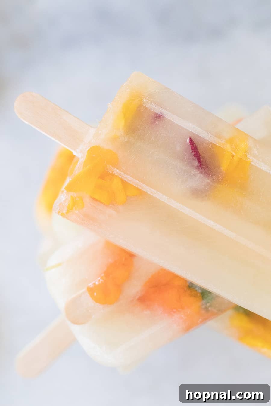 Three Ingredient Honey Lemonade Popsicles with edible flowers and lemons on a marble table, a close-up.