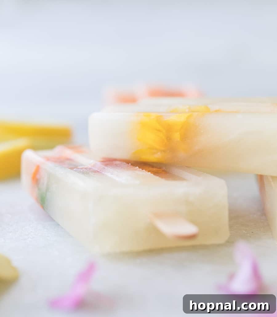 Three Ingredient Honey Lemonade Popsicles with edible flowers and lemons on a marble table, artfully arranged.