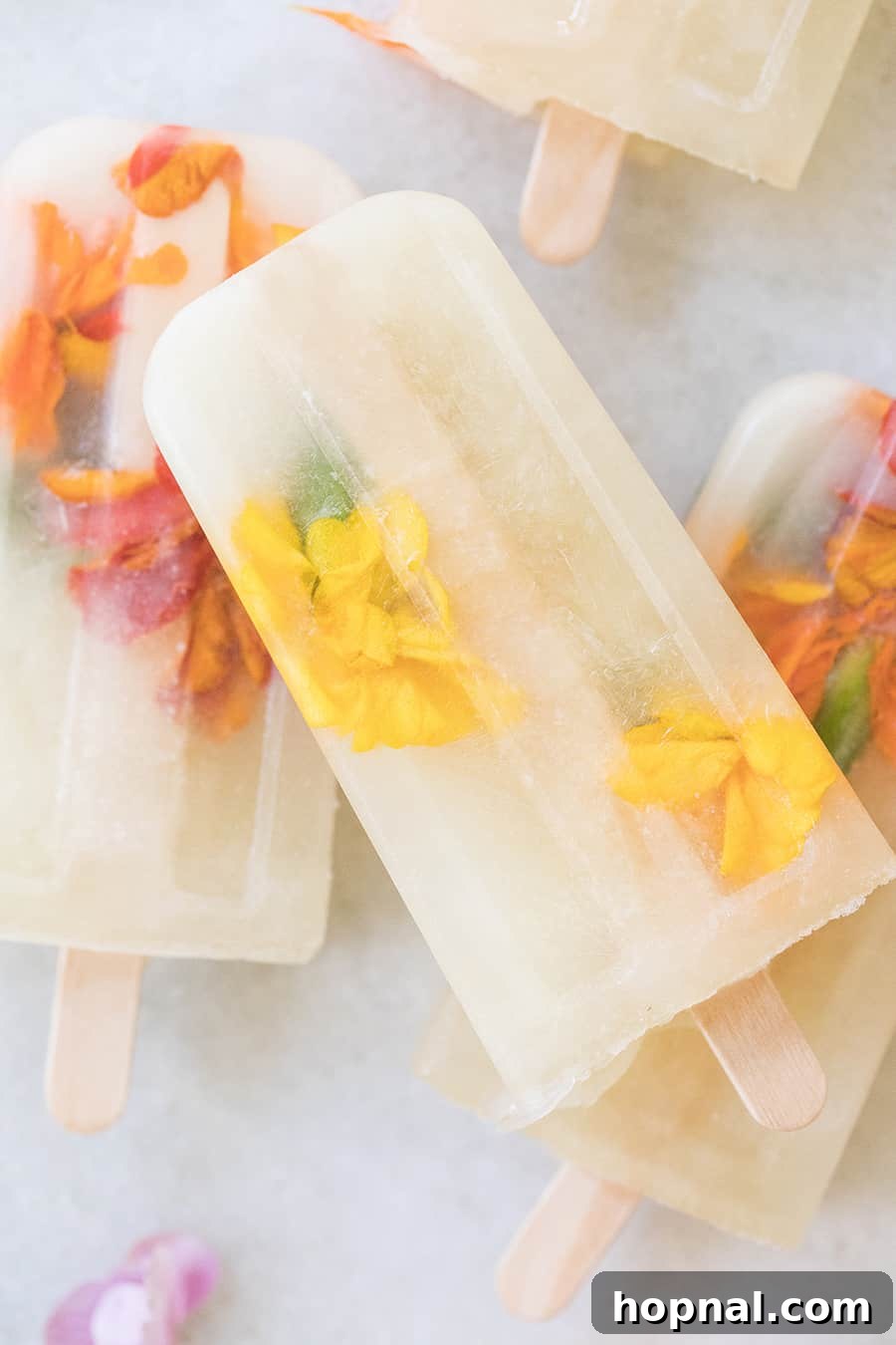 Three Ingredient Honey Lemonade Popsicles with edible flowers and lemons on a marble table, a final aesthetic shot.