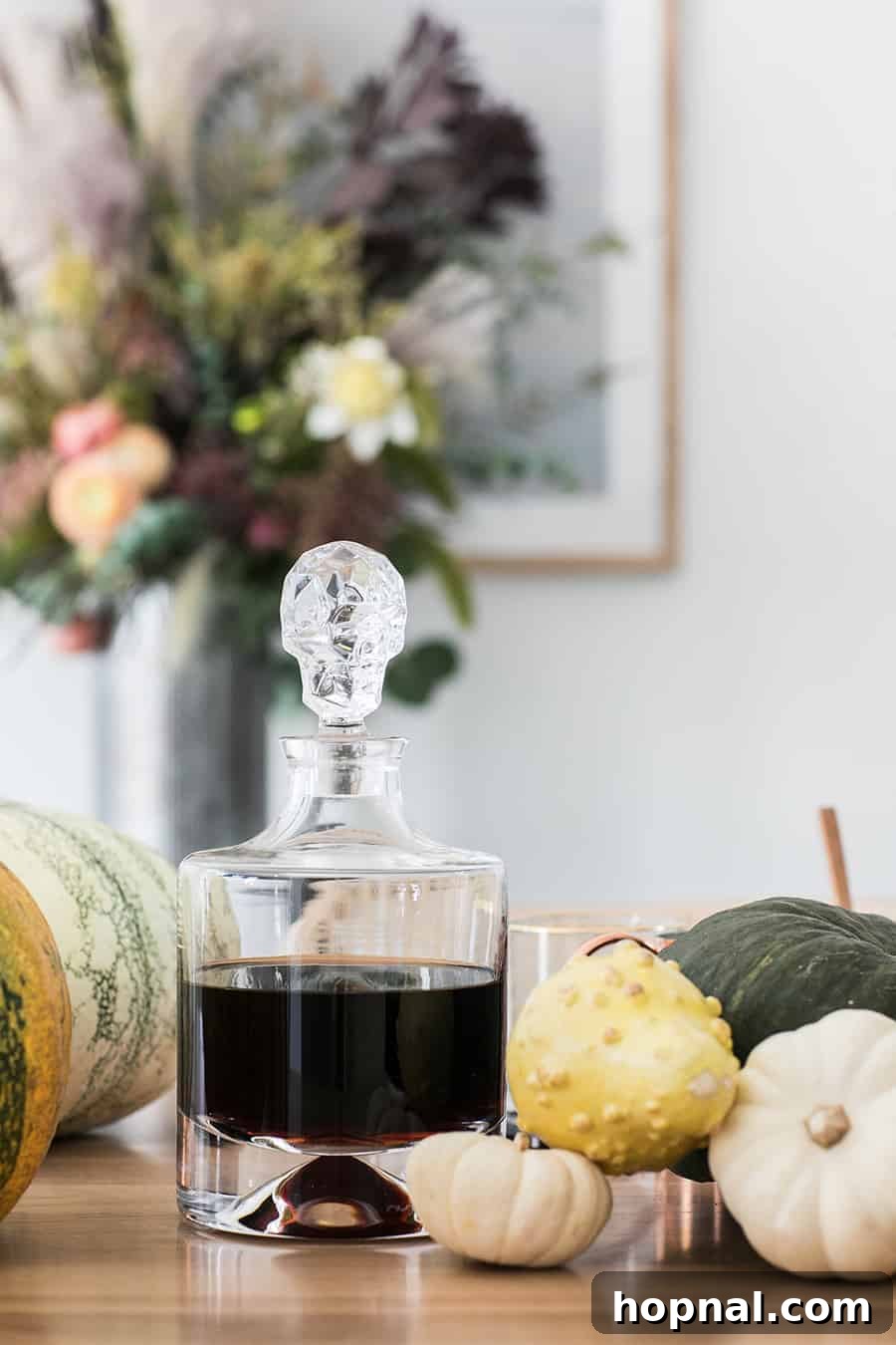 An elegant skull decanter filled with dark rum, positioned next to pumpkins on a beautifully decorated table.