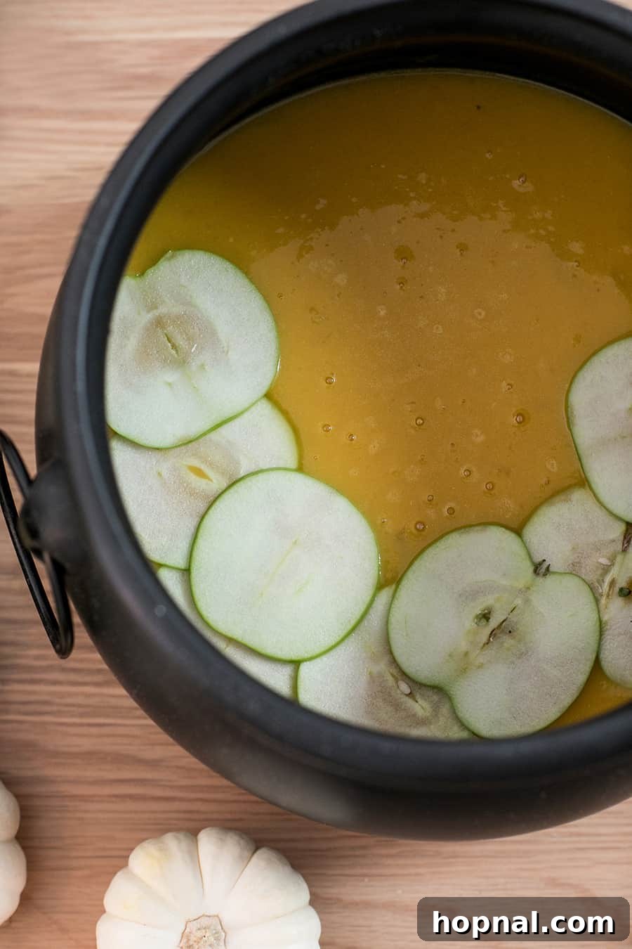 Top-down shot of vibrant curried butternut squash soup served in a black cauldron, garnished with green apple slices.