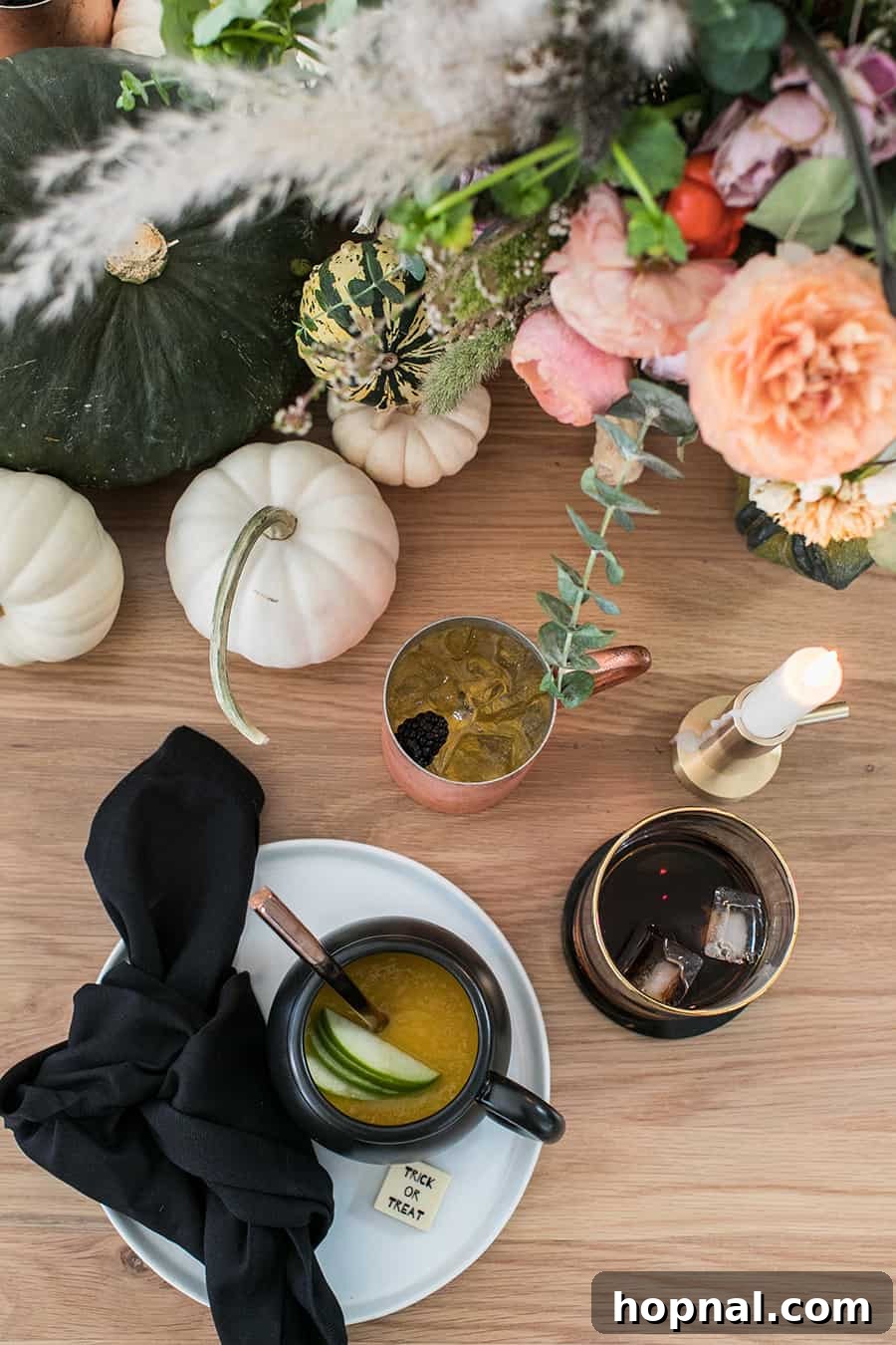 Halloween dinner ideas with the centerpiece featuring soup in a cauldron, surrounded by pumpkins, flowers, and candles, creating a cozy and elegant table.