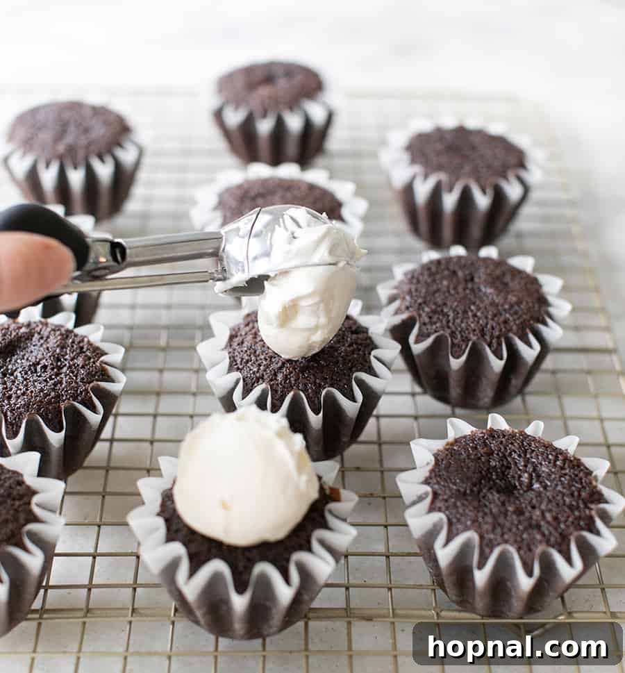 Scooping fluffy buttercream frosting onto a freshly baked chocolate cupcake for decoration