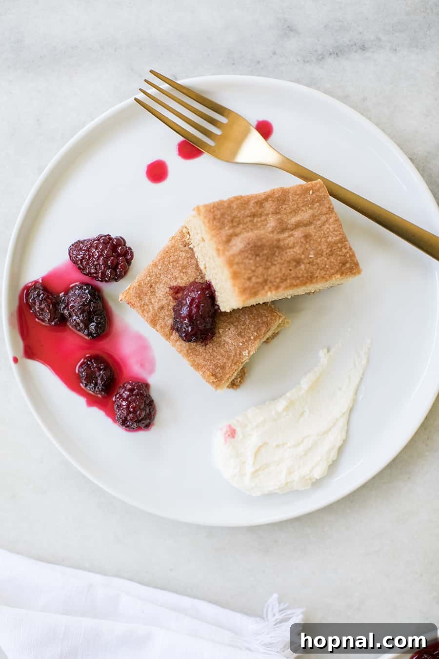 A slice of golden brown sugar cake on a white plate, garnished with fresh blackberries.