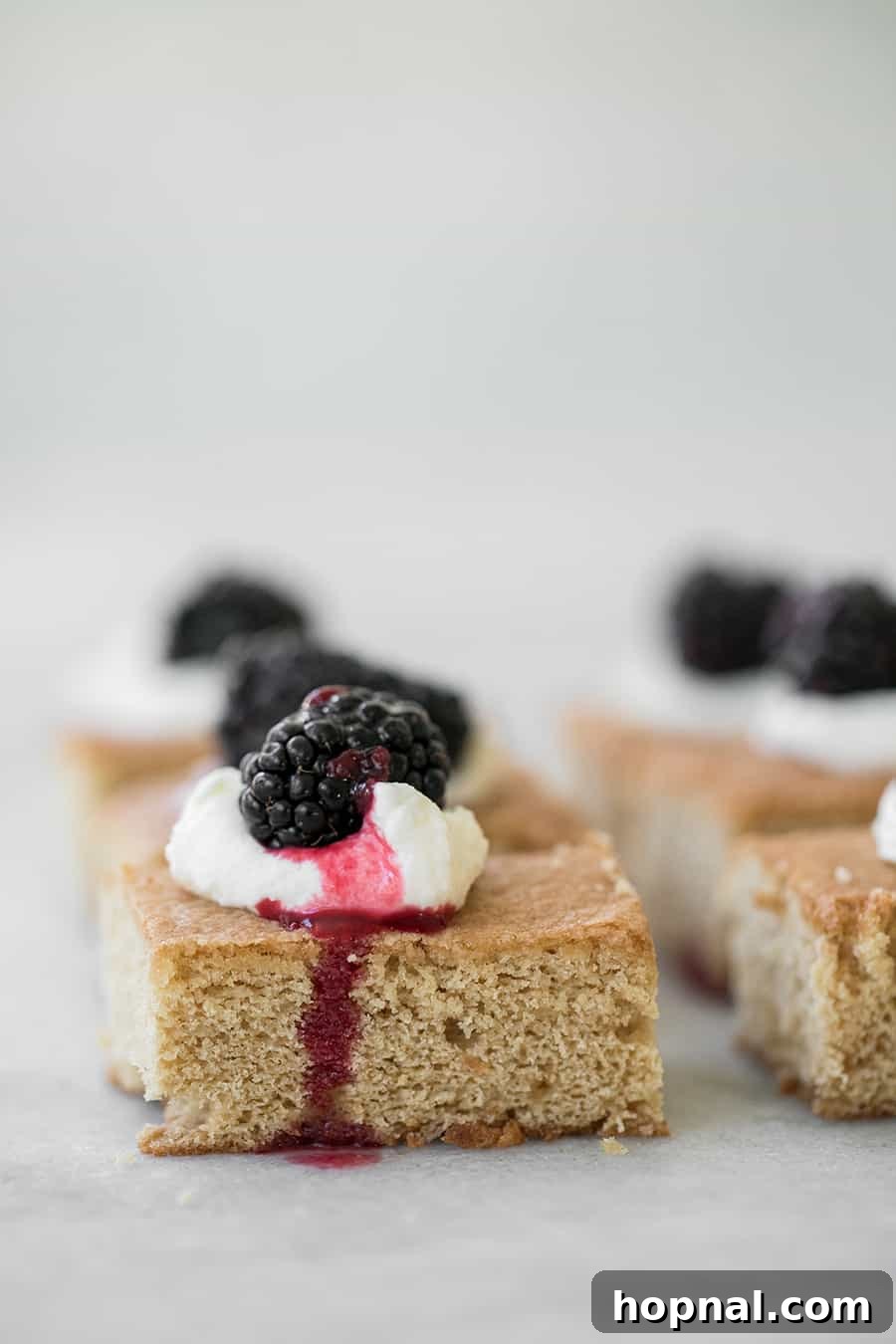 Brown sugar cake topped with a dollop of whipped cream or crème fraîche and a single fresh blackberry.