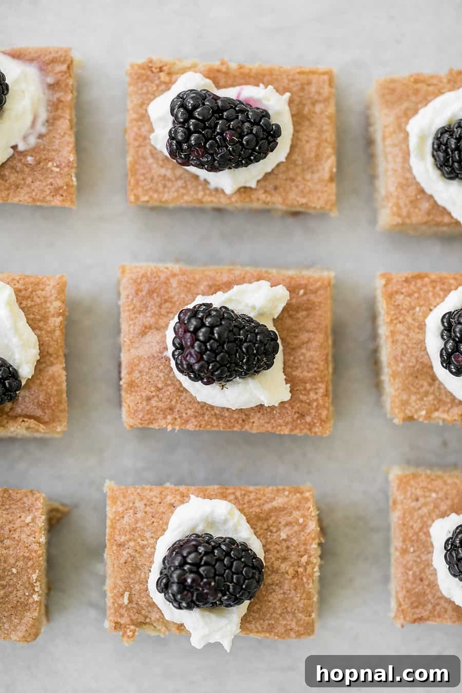 Brown sugar cake cut into neat squares, with several fresh blackberries scattered around.