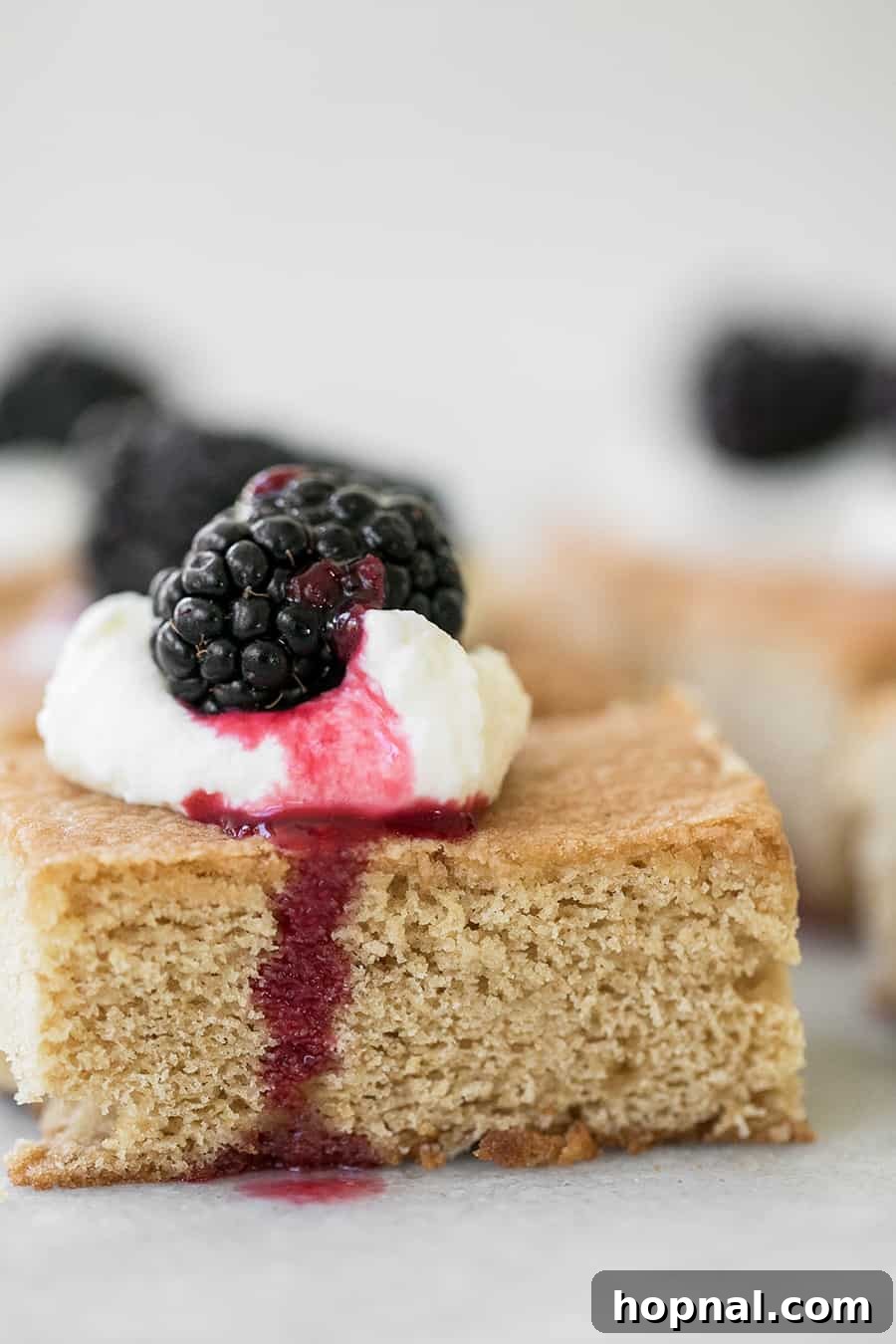 Close-up of a brown sugar cake slice with a generous dollop of crème fraîche and a fresh blackberry on top.