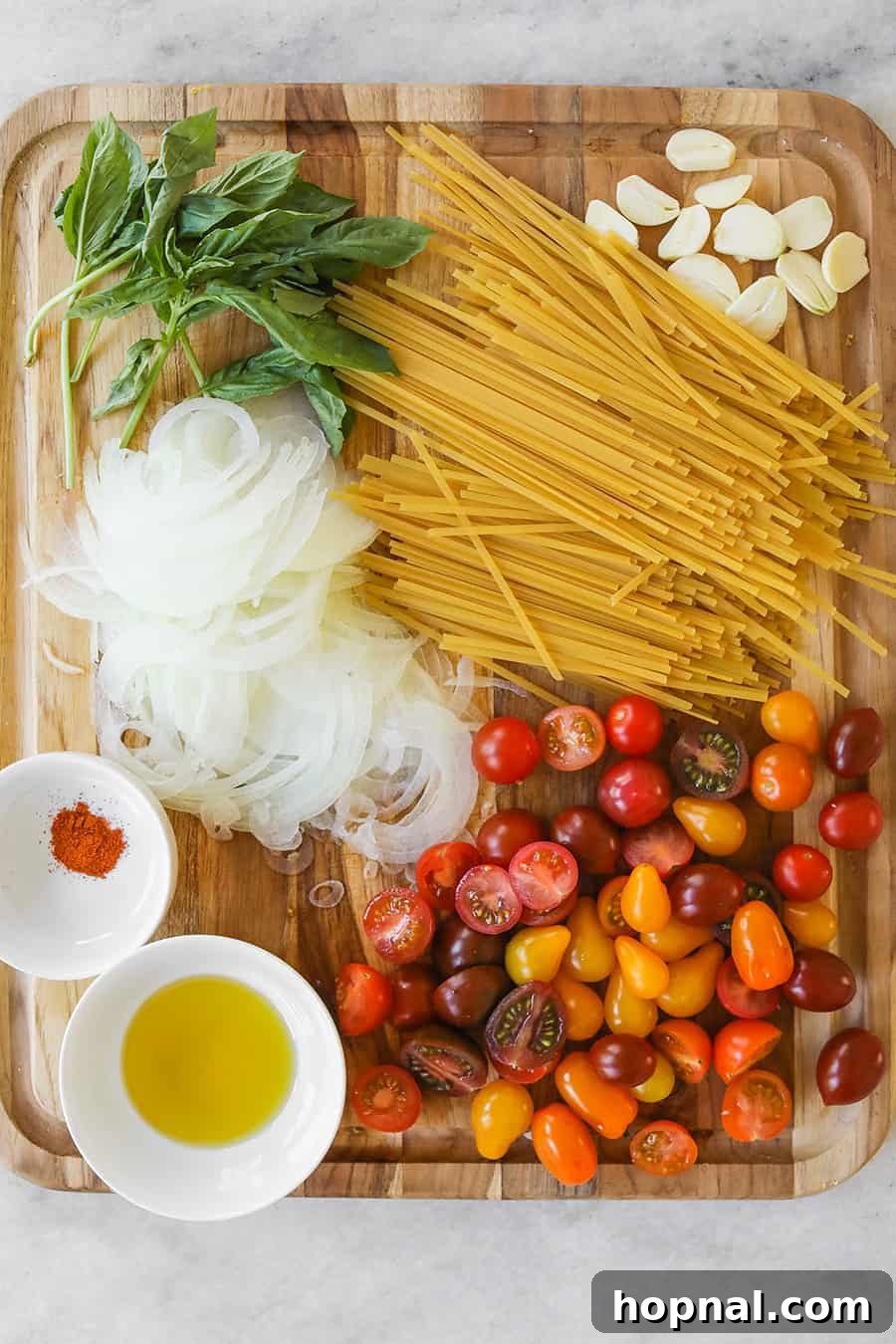 Fresh ingredients laid out for one pan pasta: red onions, cherry tomatoes, garlic cloves, fresh basil, and dry linguine pasta.