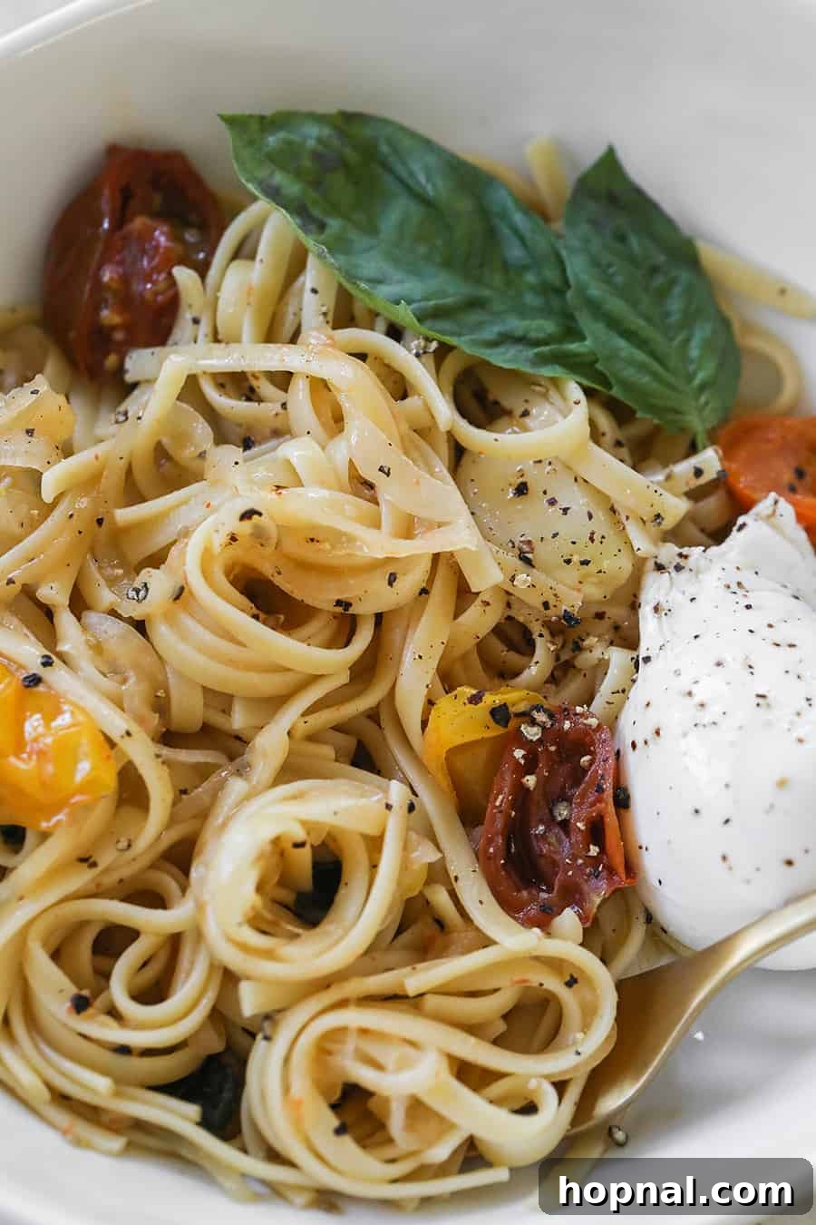 A close-up shot of the cooked One Pan Basil and Tomato Pasta, highlighting the glossy noodles, burst tomatoes, and fresh basil leaves, ready to be served.