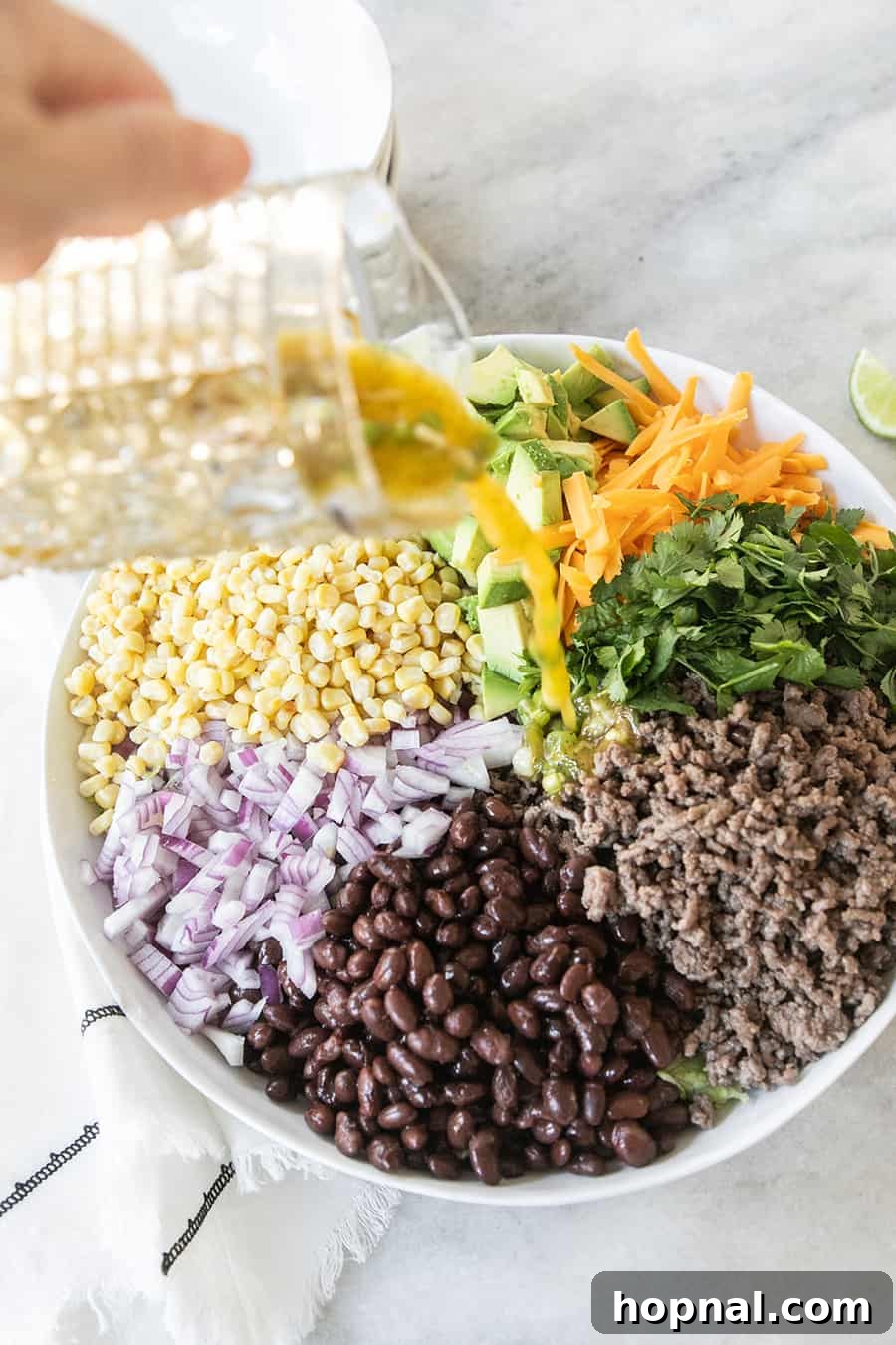 Southwest Fiesta Salad 5 Vibrant citrus dressing being poured generously over a bowl of ground beef, beans, cheese, corn, and red onions in a taco salad.
