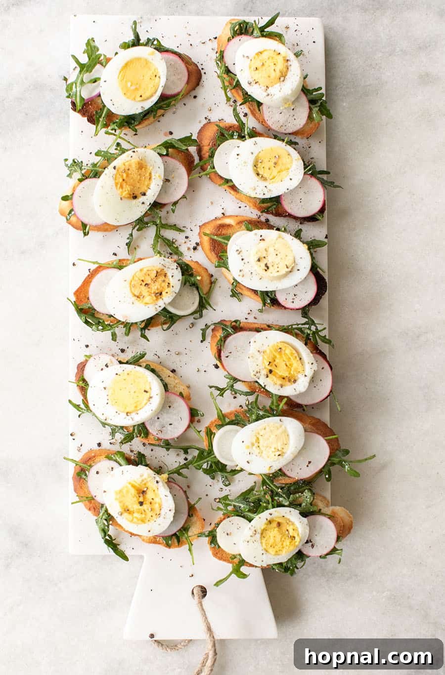 Gourmet Hard-Boiled Egg Crostini Bites 2 Crostini recipe with hard boiled eggs, arugula, salt and pepper. A close-up view of a beautifully arranged crostini.