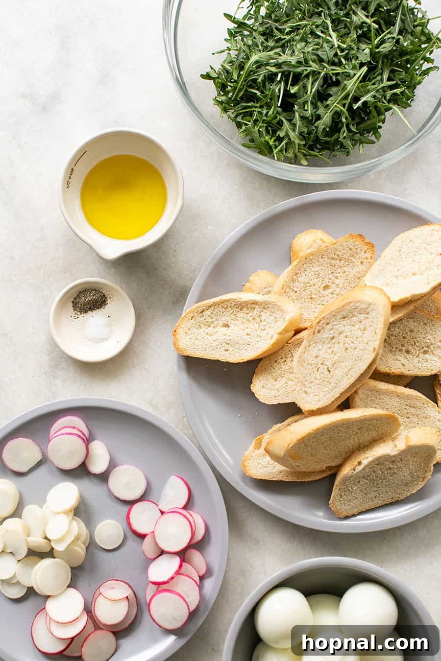 Gourmet Hard-Boiled Egg Crostini Bites 4 Ingredients to make a crostini recipe. Layed out ingredients include eggs, radishes, arugula, olive oil, and a baguette.