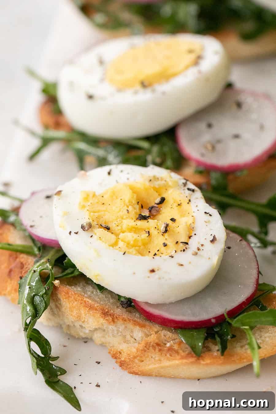 Gourmet Hard-Boiled Egg Crostini Bites 6 Hard boiled egg crostini with salt and pepper. A close-up shot of the crostini, highlighting the toppings and seasoning.