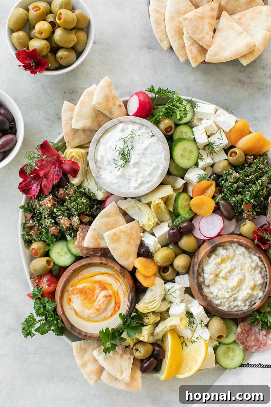 Close-up of a rustic Greek mezze platter overflowing with creamy hummus, salty feta, assorted olives, and warm pita bread triangles.