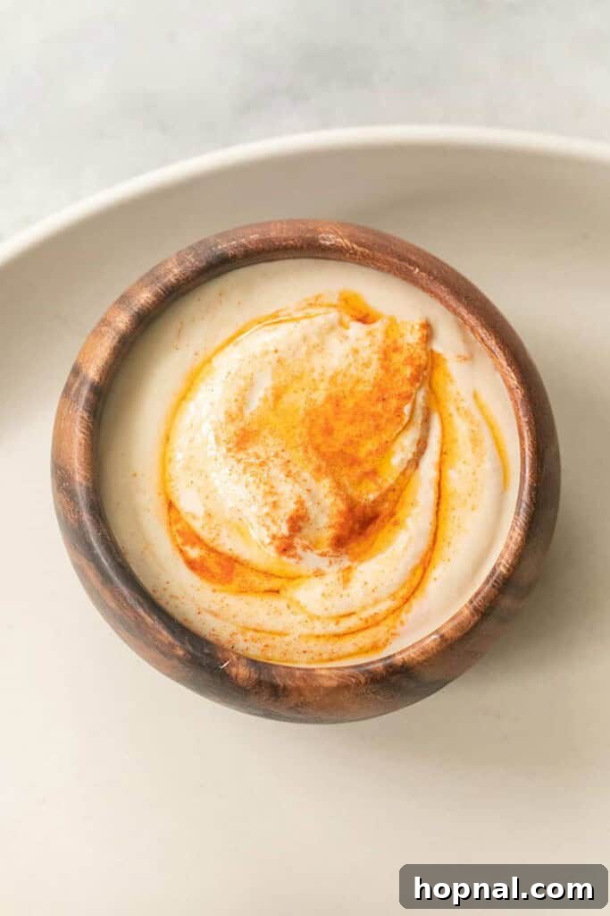 Close-up of creamy hummus dip, garnished with olive oil and spices, on a Greek mezze platter.