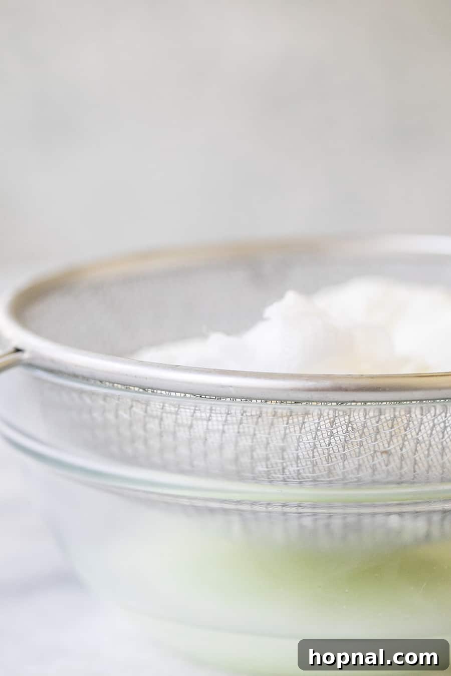 Organic whole milk yogurt being carefully poured into a cheesecloth-lined strainer over a clear bowl, illustrating the draining process for homemade labneh.