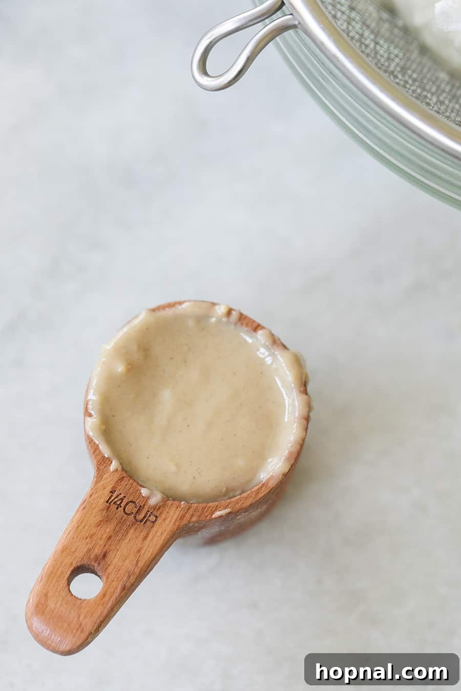 A quarter cup of creamy tahini paste in a small wooden measuring cup, ready to be added to the yogurt dip.