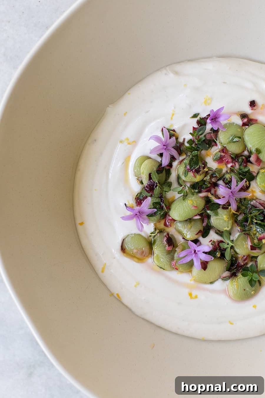 A beautifully presented bowl of creamy tahini yogurt dip, generously topped with an artful arrangement of lima beans, fresh thyme, lemon zest, and a drizzle of olive oil, ready to be served.