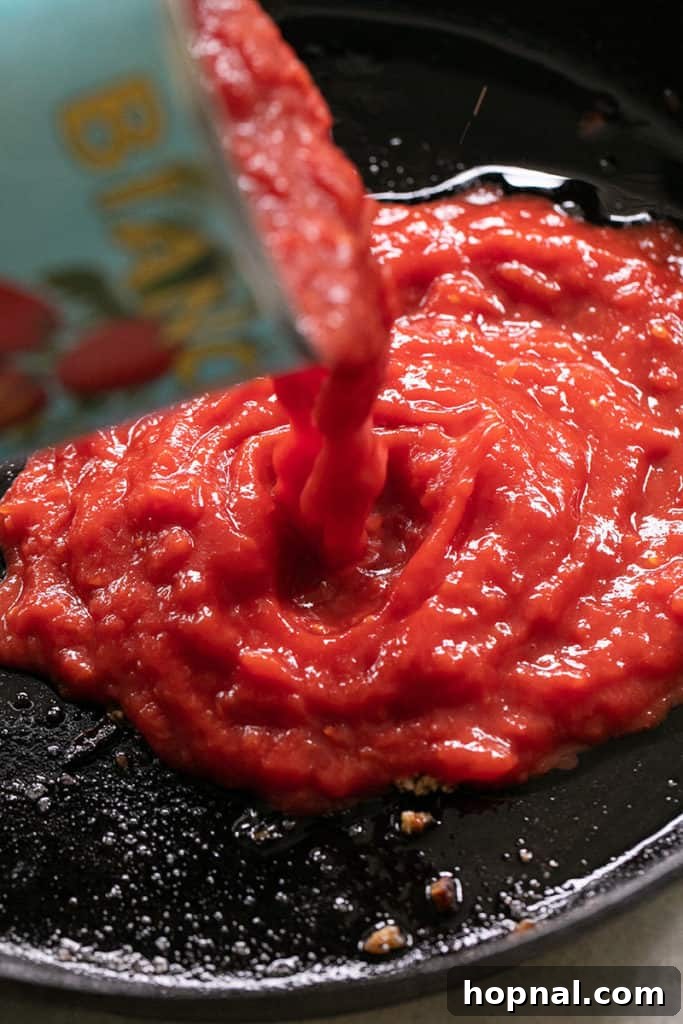 Savory Turkey Meatball Delights 9 Can of crushed tomatoes being poured into a cast iron skillet, suggesting a sauce addition.