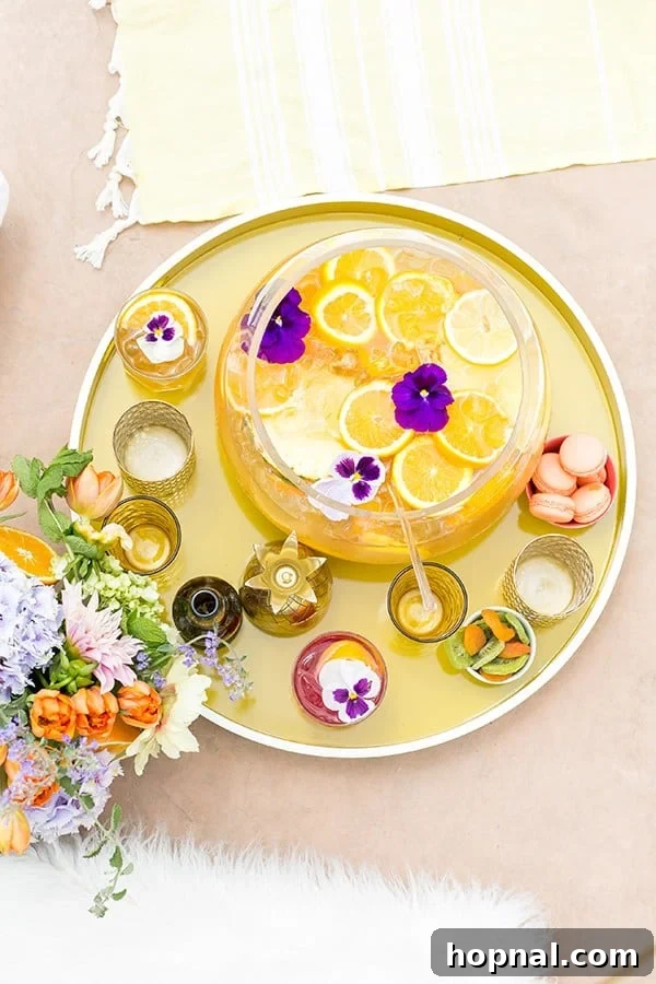 Pineapple party punch in bowl with orange slices on a yellow tray with flowers and pretty summer cups.