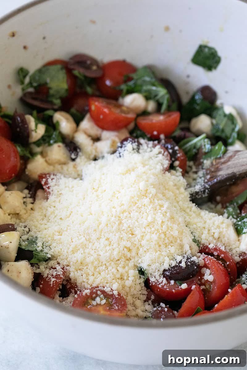 Parmesan cheese being sprinkled into a generous bowl of summer pasta salad, highlighting its rich texture. 